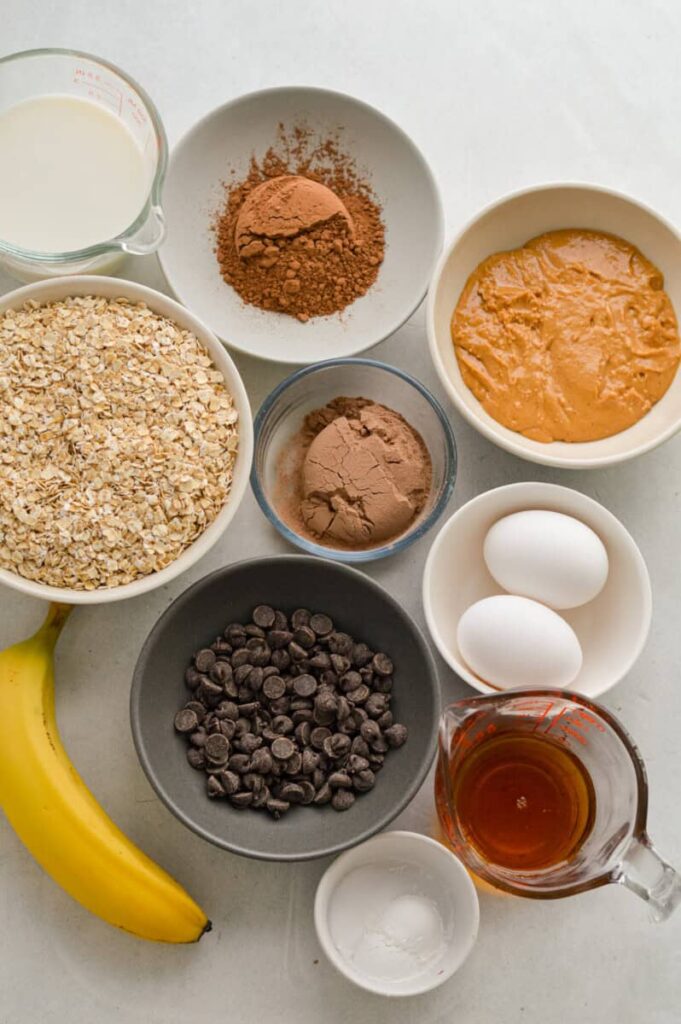 ngredients for chocolate baked oat cups including oats, cocoa, banana, eggs, and chocolate chips